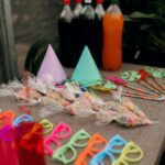 Vibrant party supplies including colorful glasses, hats, and soda bottles on a table.