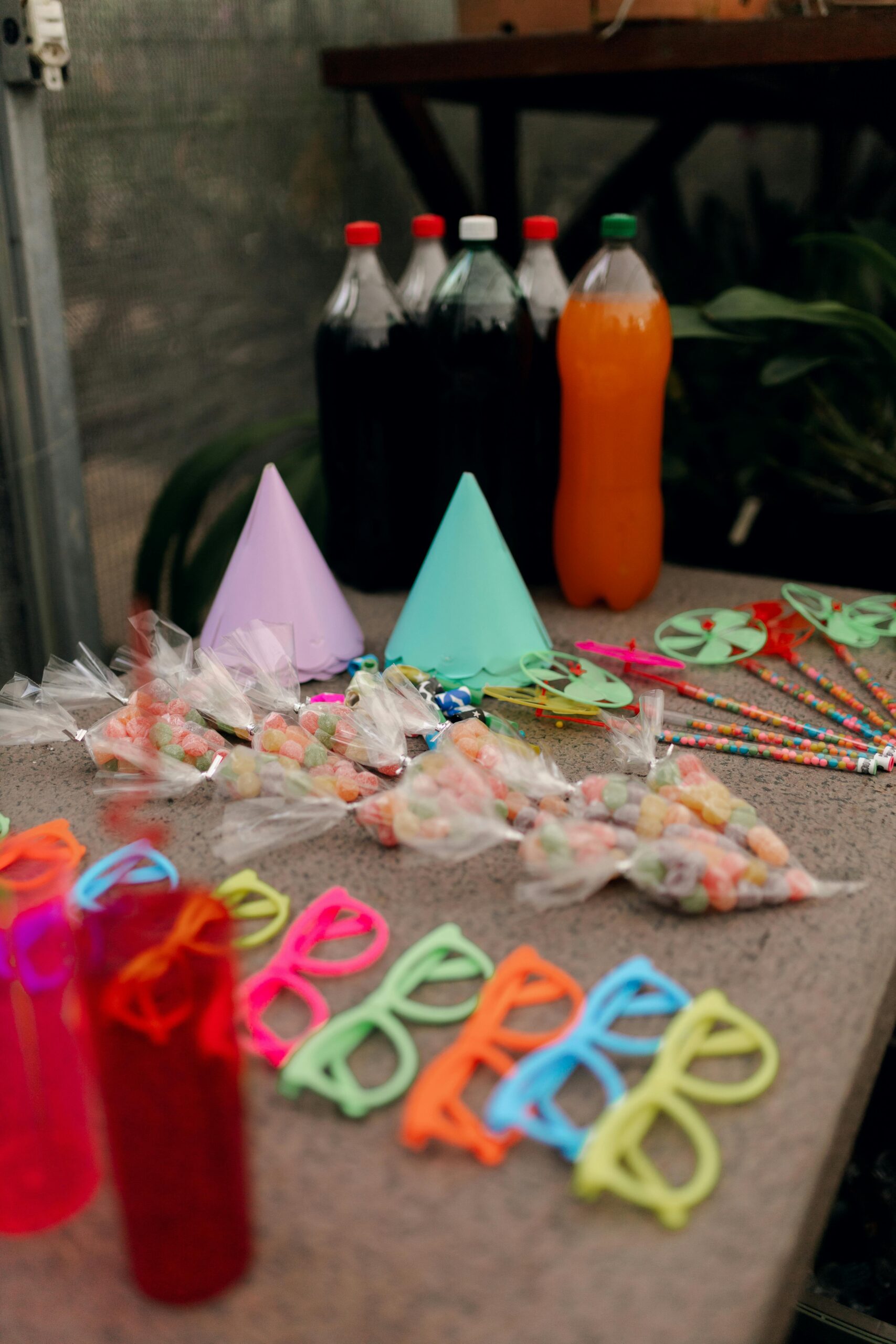 Vibrant party supplies including colorful glasses, hats, and soda bottles on a table.